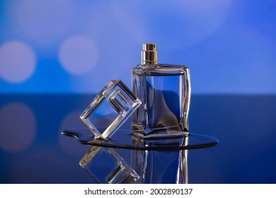 Unbranded Perfume Bottle On Glassy Surface, Blurred Blue Background. Beauty And Product Photography Concept