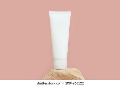 Unbranded white squeeze bottle cosmetic tube on stone on pink background.  Mockup with copy space. Cream bottle for branding and label, front view, closeup. Natural organic spa cosmetics.