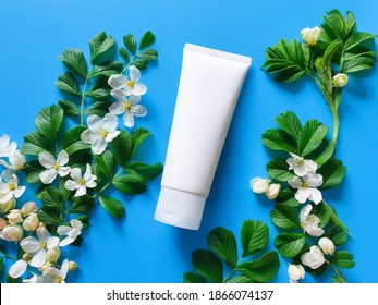 Unbranded White Squeeze Cosmetic Tube, Spring Flowers And Leaves On Bright Blue Background. Natural Organic Spa Cosmetics Concept. Flatlay Lifestyle, Mockup, Top View.