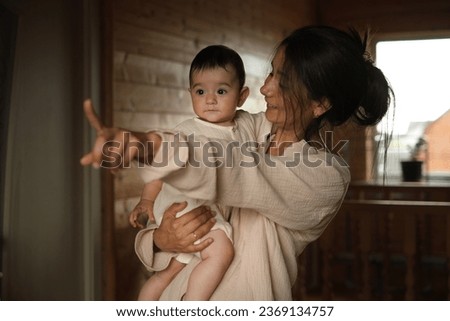Unbreakable Bond Between a Smiling Young Mother and Her Year-Old Daughter, Celebrated in Their Warm Wooden Sanctuary
