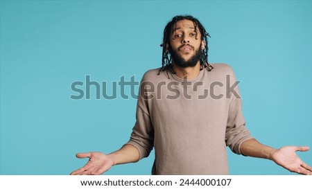 Uncaring Middle Eastern man shrugging shoulders, showing indifference and apathy. Careless BIPOC person doing nonchalant indifferent hand gesturing, isolated over studio background, camera A