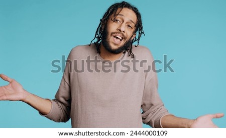 Uncaring Middle Eastern man shrugging shoulders, showing indifference and apathy. Careless BIPOC person doing nonchalant indifferent hand gesturing, isolated over studio background, camera B
