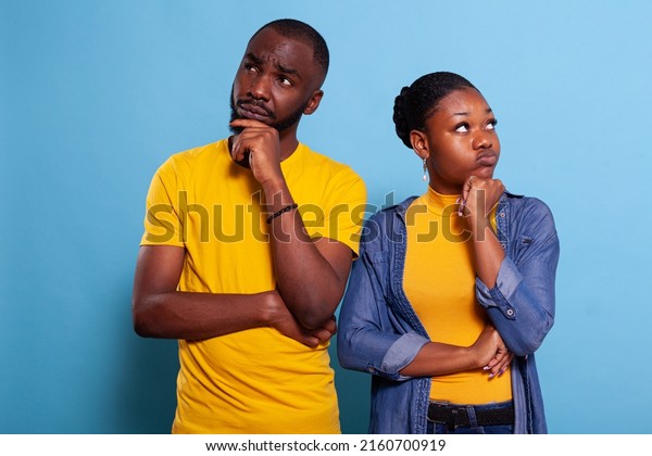 Uncertain couple thinking about clever\
decision in studio. Pensive and thoughtful lovers brainstorming new\
solution for success, looking sideways and holding chin with hand\
in contemplation.