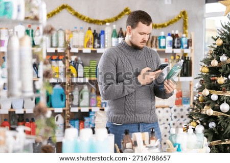 Uncertain middle-aged guy scanning barcode on dishwashing liquid in household goods shop during Christmas