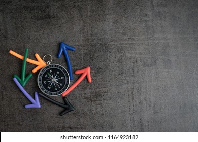 Uncertain path or multiple random life fortune and directions concept, compass at the center with magnet arrows pointing random multi directions on dark black chalkboard cement wall with copy space.
