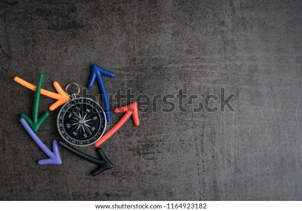 Uncertain path or multiple random life fortune and\
directions concept, compass at the center with magnet arrows\
pointing random multi directions on dark black chalkboard cement\
wall with copy space.