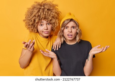 Uncertain women spread palms stand indignant cannot make decision shrug shoulders wear casual t shirts isolated over yellow background. Unsure hesitant female models feel questioned and clueless