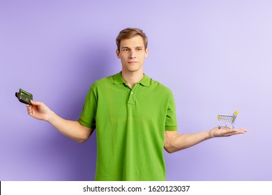 Uncertain Young Caucasian Man Holding Toy Truck And Wallet In Hands, Wearing Green T-shirt And Looking Side, Can Not Choose