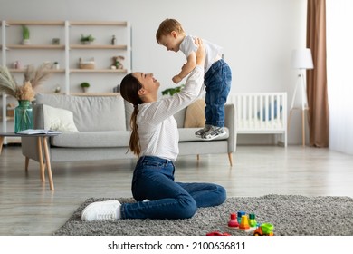 Unconditional love. Happy young mother enjoying time with her adorable toddler son at home, lifting him in the air, playing with kid boy in living room, free space