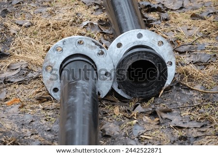Unconnected black heavy-duty plastic pipes for water pumping with joints constructed of metal. Clear bolts and screws. The pipes are located on the ground in nature. GoranOfSweden