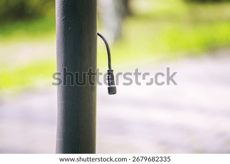 unconnected electrical wire with threaded connector protrudes from a metal park light pole, awaiting installation. 