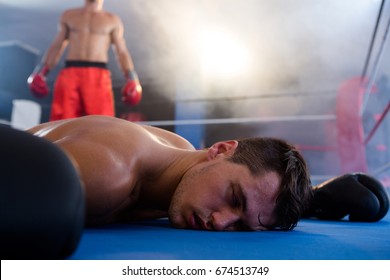 Unconscious male boxer lying by athlete in boxing ring at fitness studio - Powered by Shutterstock