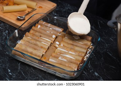 Uncooked Cannelloni Pasta In Glass Bowl With Bechamelle Sauce. Pouring White Saunce Over Cannelloni. Food Preparing Proces.