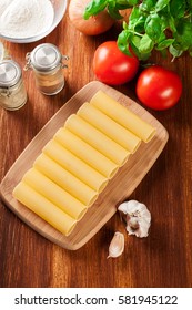 Uncooked cannelloni pasta on cutting board and ingredients. Italian cuisine. Top view