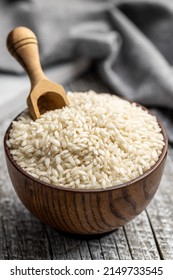 Uncooked Carnaroli risotto rice in bowl on a wooden table.