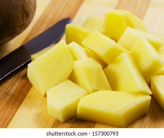 Uncooked cubical yellow potatoes on a chopping board.