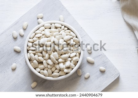 Uncooked dried white haricot beans in bowl or spoon on table. Heap of legume haricot bean background ( Phaseolus vulgaris )