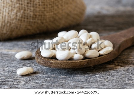 Uncooked dried white haricot beans in wooden spoon on wooden table. Heap of legume haricot bean background ( Phaseolus vulgaris )