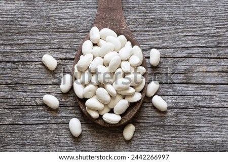 Uncooked dried white haricot beans in wooden spoon on wooden table. Heap of legume haricot bean background ( Phaseolus vulgaris )