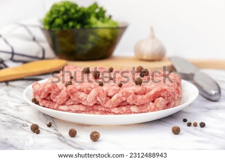 Uncooked gound pork, beef. Fresh raw minced meat with peppercorns on white plate. Ingredients for cooking meal, tomatoes, broccoli, garlic on marble table on kitchen.
