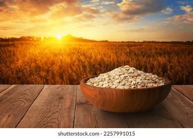 uncooked oat flakes in bowl on table with ripe cereal field on sunset as background - Shutterstock ID 2257991015
