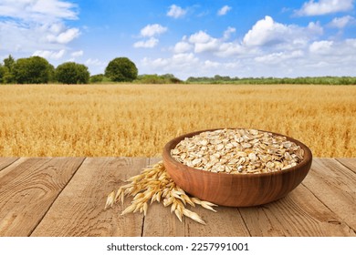 uncooked oatmeal in bowl on table with ripe cereal field on the background - Shutterstock ID 2257991001