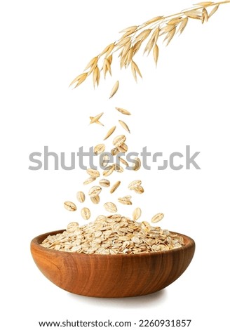 uncooked oatmeal falling from ripe oat ears in wooden bowl isolated on white background