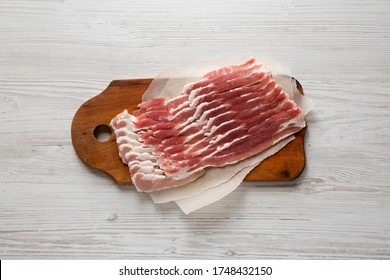 Uncooked Raw Bacon On A Rustic Wooden Board On A White Wooden Background, Top View. Flat Lay, From Above, Overhead. 