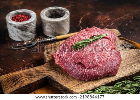 Uncooked Raw beef veal cheeks on wooden board. Dark background. Top view.