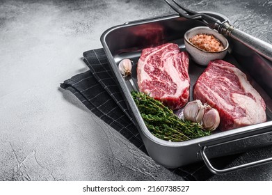 Uncooked Raw chuck eye roll steaks in a steel kitchen tray. Gray background. Top view. Copy space.