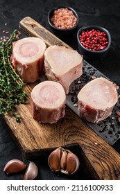 Uncooked Raw veal Marrow bones on butcher board with meat cleaver. Black background. Top view