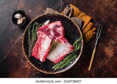 Uncooked Raw veal Short Ribs on rustic plate with rosemary. Dark background. Top view.