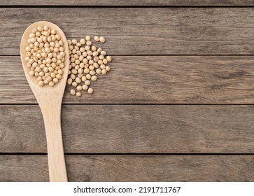 Uncooked soy beans on a sppon over wooden table with copy space.