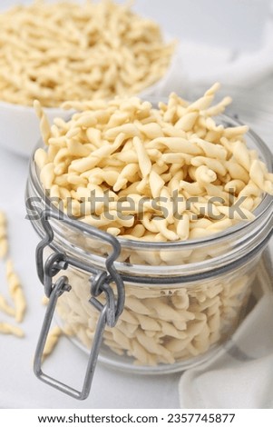 Uncooked trofie pasta in glass jar on white table, closeup