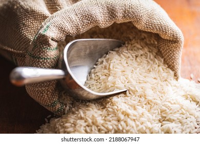 Uncooked white rice in a burlap sack on wooden table.
