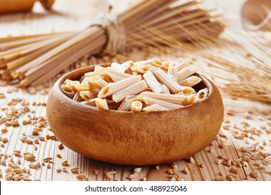 Uncooked Whole Wheat Pasta In Wooden Bowl Surrounded By Wheat Spaghetti In Background