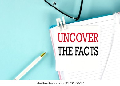 UNCOVER THE FACTS text on sticky on notebook with pen and glasses , blue background