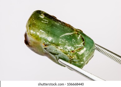 An Uncut Green Sapphire Crystal Held By Tweezers