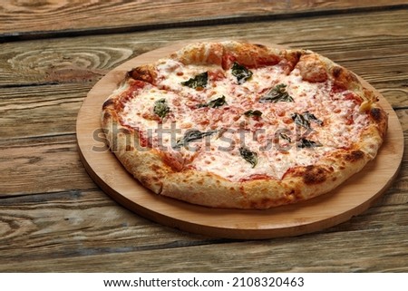 Uncut Italian pizza served with fresh basil leaf on Wooden board on dark texture background. Hot pizza with tomatoes and pesto sauce