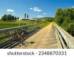Under a blue Summer sky, a red bike rests against a wooden bridge railing on the Elroy-Sparta State Trail as it passes through farm country near Sparta, WI.