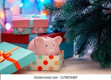 Under A Christmas Tree In A Holiday Box We Lay A Piggy Bank. A Gift, A Symbol Of The New Year. An Unusual Photo.