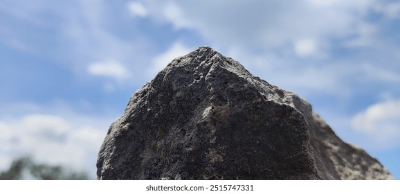 Under a clear blue sky dotted with fluffy white clouds, a rugged rock formation stands tall, adding a striking contrast and a sense of enduring natural beauty to the scene. - Powered by Shutterstock