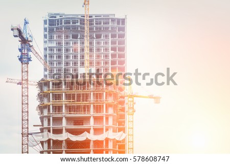 Under construction high-rise building with yellow construction crane in the sunlight
