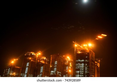 Under Construction Sky Scraper With Cranes, Working Lights Shot Against A Moonlit Cloudy Sky. One Of The Number Of Projects That Have Started In Gurgaon, Noida, Delhi, Hyderabad, Bangalore Real Estate