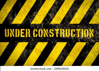 Under construction warning sign with yellow and dark stripes painted over concrete wall coarse facade as texture background. Concept for do not enter the area, caution, danger, construction site.