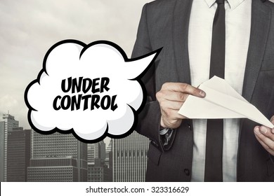Under control text on speech bubble with businessman holding paper plane in hand on city background