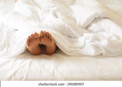 Under The Covers With Feet Showing In A Bed