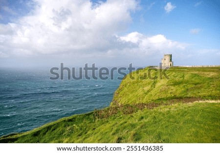 Under a dramatic cloudscape, O’Briens Tower, the stone building at the Cliffs of Moher, looks out over the wind-blown waves of the Atlantic Ocean on a sunny, summer day in County Clare, Ireland.