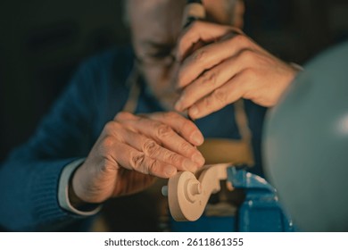 Under focused lighting in Cremona, a violin maker uses a vertical chisel to define the scroll. The scroll, blue vise, and gloved hands show traditional skill and deep dedication to the craft.