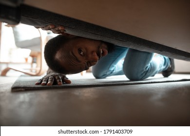 Under His Bed In Bedroom. African-american Man Looking For Job In Unusual Places At His Home. Crazy, Funny Way To Find Career And Going Up. Concept Of Crisis, Unemployment, Finance, Business.